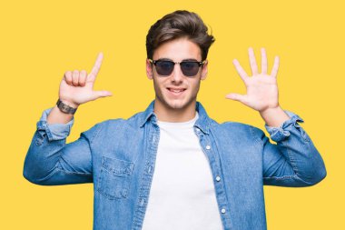 Yakışıklı delikanlı üzerinde güneş gözlüğü takıyor gösterilen arka plan izole ve parmakları ile işaret kendinden emin ve mutlu gülümseyerek süre yedi numara.