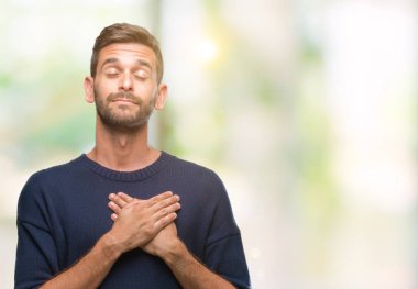 Yakışıklı delikanlı ile gülümseyen izole arka plan üzerinde kış kazak giyen kapalı gözler ve yüzünde minnettar jest ile göğüs üzerinde eller. Sağlık kavramı.