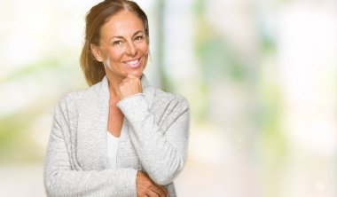 Emin çapraz kollar ve çeneme kaldırdı el ile gülümseme ile kameraya bakarak izole arka plan üzerinde kış kazak giyen güzel orta yaş yetişkin kadın. Pozitif düşünce.