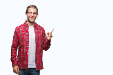 Kameraya bakarak yan el ve parmak ile işaret eden genç yakışıklı adam uzun saçlı gözlüklü yüzünde kocaman bir gülümseme ile izole arka plan üzerinde.