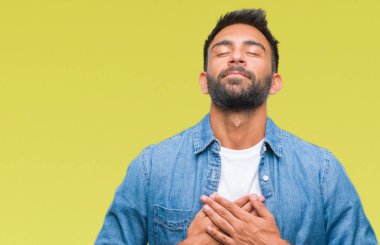 Göğüs kapalı gözler ve yüzünde minnettar jest ile yetişkin İspanyol adam ile gülümseyen izole arka plan üzerinde eller. Sağlık kavramı.