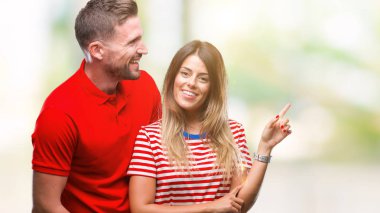 Kameraya bakarak yan el ve parmak ile işaret yüzünde kocaman bir gülümseme ile izole arka plan üzerinde aşık genç çift.