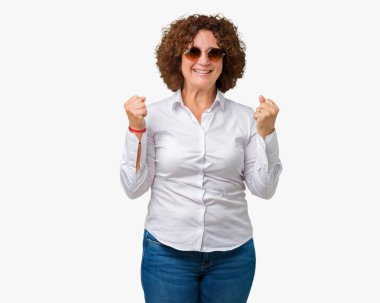 Güzel orta ager üst düzey iş kadını izole arka plan kutlama üzerinde güneş gözlüğü takıyor şaşırttı ve başarı için kaldırdı kollarını açarak hayret ve gözleri açık. Kazanan kavramı.