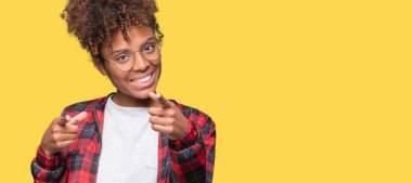 Fotoğraf makinesi ile mutlu ve komik yüz için parmakları işaret izole arka plan üzerinde gözlük güzel genç Afro-Amerikan kadın. İyi enerji ve vibes.