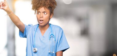 İzole arka plan ile sürpriz devam et, parmakla üzerinde genç Afro-Amerikan doktor kadın ağzı açık ifade, önünde bir şey hayret