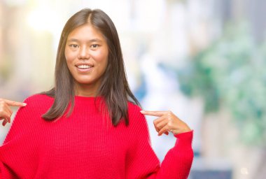 Yüzünde gülümseme ile kendinden emin görünüyorsun, kendini gururlu ve mutlu parmakları ile işaret izole arka plan üzerinde kış kazak giyen genç Asyalı kadın.