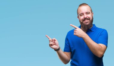 Gülümseyen ve iki elleri ve parmakları ile tarafına işaret kamera bakarak izole arka plan üzerinde mavi gömlek giymiş genç beyaz hipster adam.