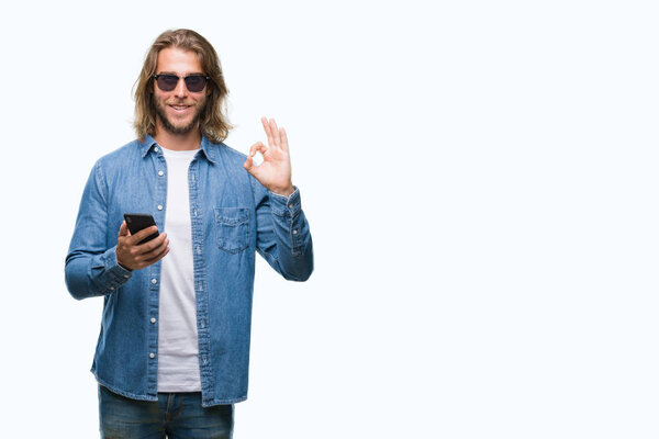 Young handsome man with long hair over isolated background sending message using smartphone doing ok sign with fingers, excellent symbol