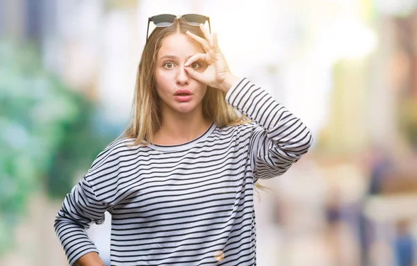 のジェスチャーを行う分離の背景の上にサングラスをかけている若い美しいブロンドの女性は 驚いた顔 指の間から見て目にショックを受けた 疑うような式 — ストック写真