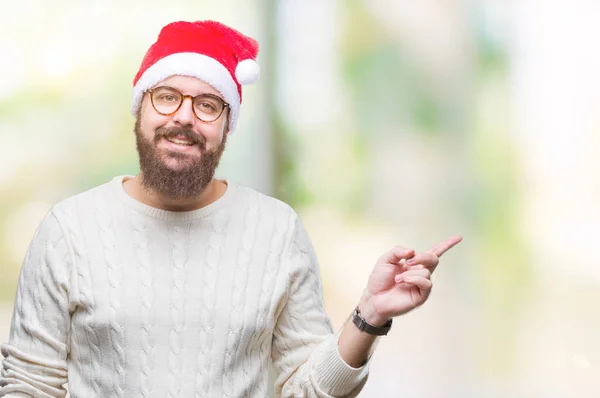 年轻的高加索男子戴着圣诞帽 戴着眼镜在孤立的背景上 脸上带着灿烂的笑容 用手和手指指着一边看着镜头 — 图库照片
