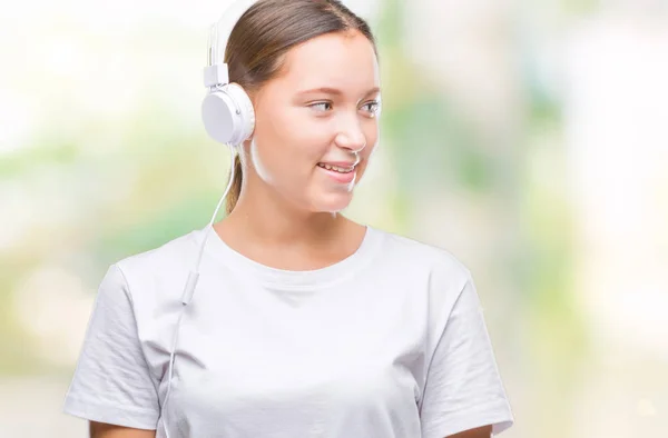 年轻的白种人妇女听音乐戴着耳机在孤立的背景看一边与微笑的脸上 自然的表达 笑的自信 — 图库照片
