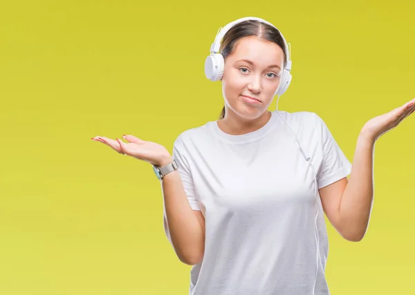 上のヘッドフォンを着て音楽を聴く若い白人女性は 腕と手を上げて背景無知と混乱式を分離しました 疑いのコンセプト — ストック写真