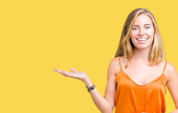 陽気な提示とカメラを見て手の手のひらで指している笑みを浮かべて分離の背景にオレンジ色のシャツを着ての美しい若い女性 — ストック写真