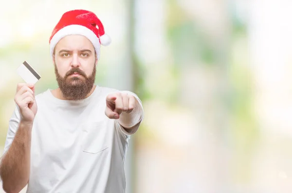 若い白人男着てクリスマス帽子保有クレジット カード カメラと指で指している孤立した背景に 手に署名 正面からポジティブで自信のジェスチャー — ストック写真