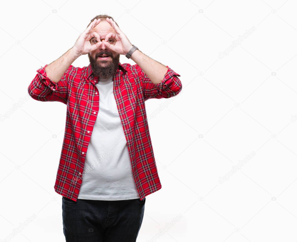 Young caucasian hipster man wearing glasses over isolated background doing ok gesture like binoculars sticking tongue out, eyes looking through fingers. Crazy expression.