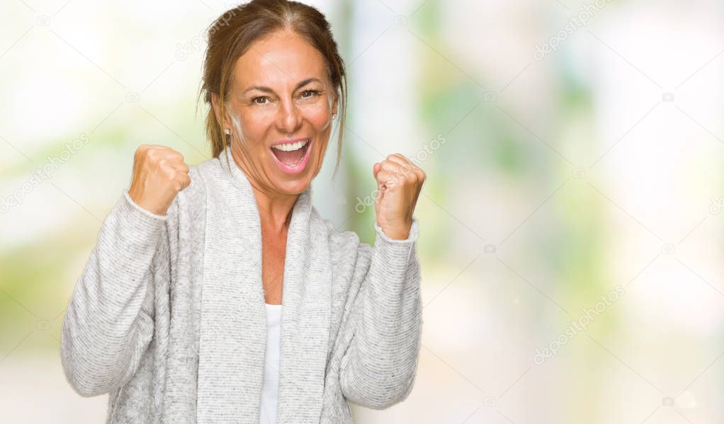 Beautiful middle age adult woman wearing winter sweater over isolated background very happy and excited doing winner gesture with arms raised, smiling and screaming for success. Celebration concept.