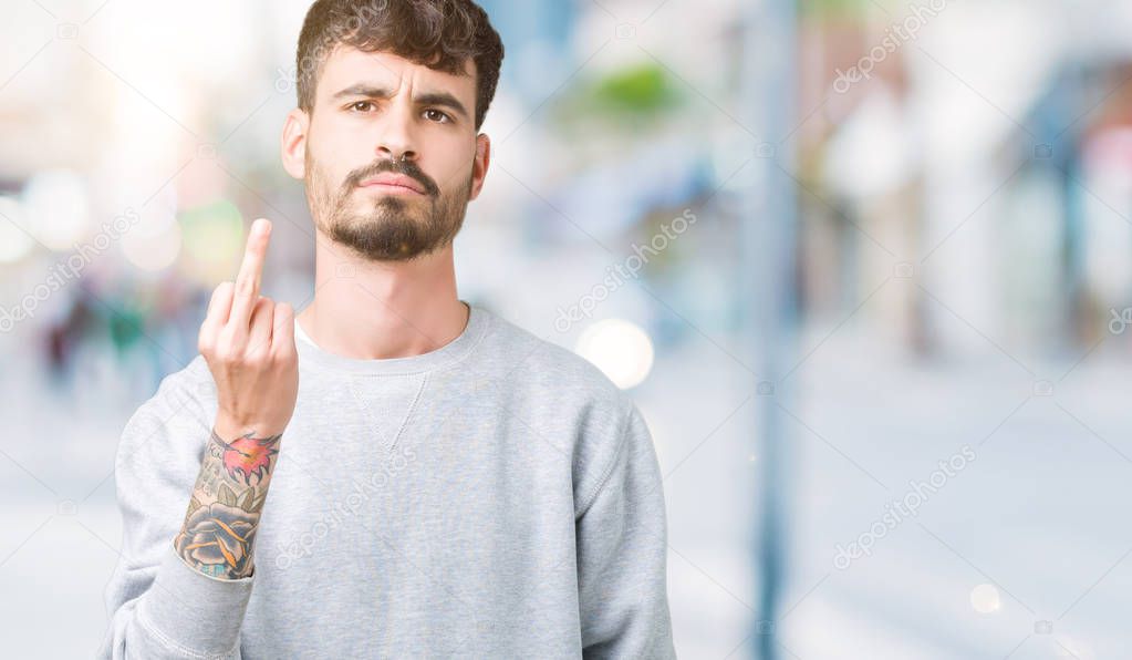 Young handsome man wearing sweatshirt over isolated background Showing middle finger, impolite and rude fuck off expression