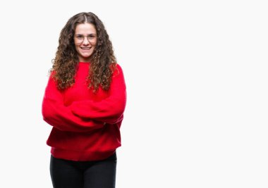 Güzel esmer kıvırcık saçlı Genç kız kameraya bakarak çapraz silah ile gülümseyen izole arka plan mutlu yüzüne gözlük ve kış kazak giyiyor. Olumlu bir kişi.