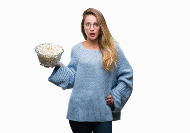 Genç güzel sarışın kadın izole arka şok sürpriz yüzü, korkuyor ve korku ifadesi ile heyecanlı olan korkmuş üzerinde patlamış mısır yemek