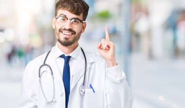 Genç başarılı fikirle parmağı yukarıyı izole arka plan üzerinde hastane ceket giyen adam doktor. Çıktıktan ve mutlu. Bir numara.