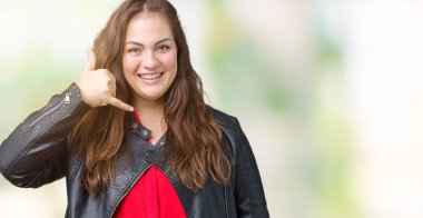 Artı boyutu genç kadın yapıyor gülümseyen izole arka plan üzerinde bir moda deri ceket giymiş güzel telefon hareketi ile el ve parmak telefonda konuşuyor gibi. Kavramları iletişim.