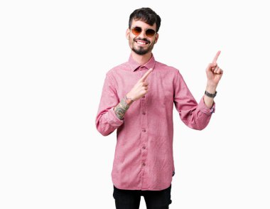 Yakışıklı delikanlı gülümseyen ve iki elleri ve parmakları ile tarafına işaret kamera bakarak izole arka plan üzerinde güneş gözlüğü takıyor.