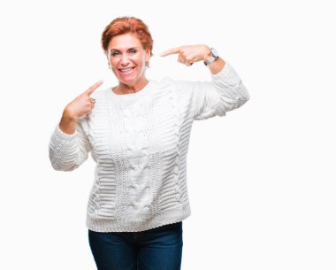 Kendinden emin gösterilen ve işaret parmakları diş ve ağız ile gülümseyen izole arka plan üzerinde kış kazak giyen Atrractive üst düzey beyaz Kızıl saçlı kadın. Sağlık kavramı.