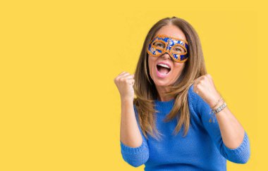 Üzerine Venedik karnaval maskesi giyen güzel orta yaş kadın gülümseyerek ve başarı için çığlık arka plan çok mutlu ve heyecanlı kaldırdı, silah ile kazanan jest yapıyor izole. Kutlama kavramı.