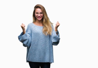 Kazak ve gözlük izole arka plan kutlama üzerinde giyen genç güzel sarışın kadın şaşırttı ve başarı için kaldırdı kollarını açarak hayret ve gözleri açık. Kazanan kavramı.