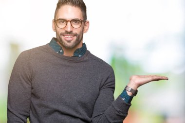 Neşeli sunulması ve kameraya bakarak avucunun ile işaret gülümseyen izole arka plan üzerinde gözlük takan genç yakışıklı adam.