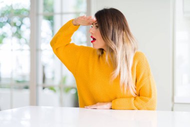 Kış kazak evde çok mutlu ve gülümseyen uzakta el ile üzerine kafa seyir giyen genç güzel kadın. Arama kavramı.