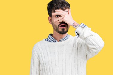 Mahcup ifadeyle parmaklarımın arasından seyir yüz ve gözler el ile kapsayan şok bakmak izole arka plan üzerinde kış kazak giyen genç yakışıklı adam.