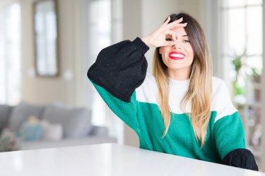 Genç güzel kadın giyiyor kış kazak evde el gülümseyen, ok jest yapıyor göz parmakları ile mutlu yüz üzerinden seyir.