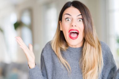 Evde kış kazak giyen genç güzel kadın deli ve başarı için hayran kaldırdı kollarını açarak kutluyor ve heyecanlı çığlık gözleri açık. Kazanan kavramı