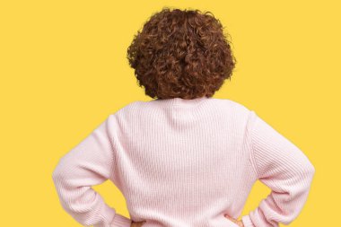 Pembe kazak ve güneş gözlüğü izole arka plan ayakta geriye doğru uzakta silah ile vücut üzerinde seyir üzerinde giyen güzel orta ager üst düzey kadın