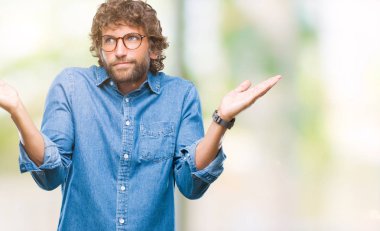 Üzerinde gözlük takan yakışıklı İspanyol model adam arka plan clueless ve şaşkın bir ifadeyle kollar ve eller kaldırdı izole. Şüphe kavramı.