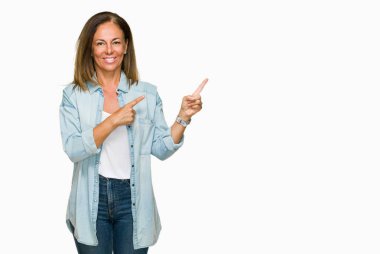 Kameraya bakarak yan el ve parmak ile işaret yüzünde kocaman bir gülümseme ile izole arka plan üzerinde rahat kot gömlek giymiş orta yaş yetişkin kadın.