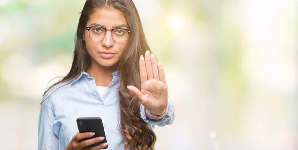 年轻美丽的阿拉伯妇女发短信使用智能手机在孤立的背景下 张开手做停止标志认真和自信的表达 防御姿态 — 图库照片