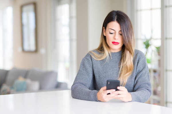 Young beautiful woman using smartphone at home with a confident expression on smart face thinking serious