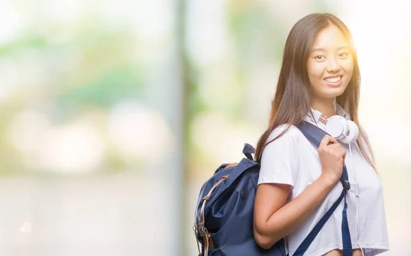 Young asian woman wearing backpack and headphones over isolated background with a happy face standing and smiling with a confident smile showing teeth