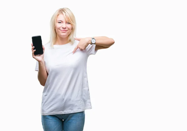 年轻美丽的金发女子显示屏幕的智能手机在孤立的背景与惊讶的脸指向自己的手指 — 图库照片