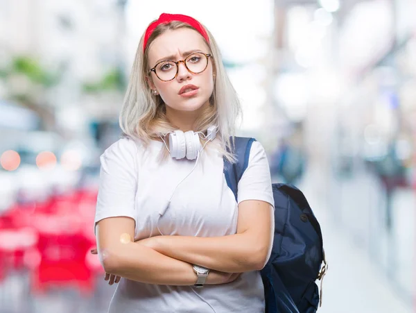 Young blonde student woman wearing glasses and backpack over isolated background skeptic and nervous, disapproving expression on face with crossed arms. Negative person.