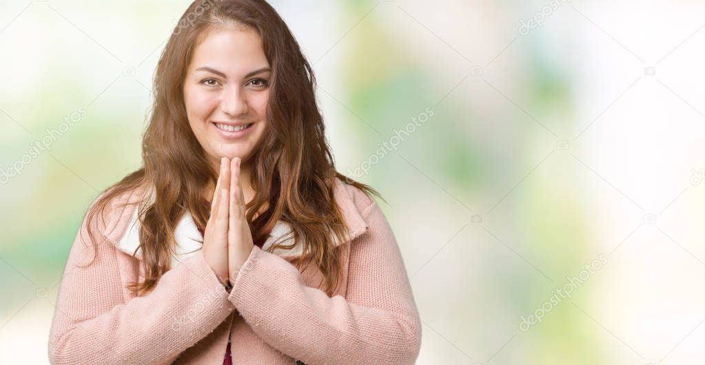 Beautiful plus size young woman wearing winter coat over isolated background praying with hands together asking for forgiveness smiling confident.