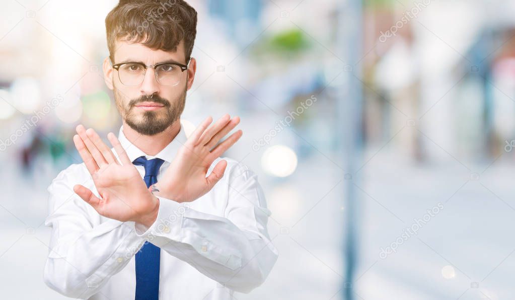 Young handsome business man wearing glasses over isolated background Rejection expression crossing arms and palms doing negative sign, angry face