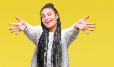 Genç örgülü saç Afro-Amerikan kız sarılmak için kollarını açarak gülümseyerek kameraya bakarak izole arka plan üzerinde kazak giyiyor. Neşeli ifade kucaklayan mutluluk.