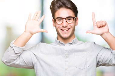 Gösterilen arka plan üzerinde gözlük takan genç yakışıklı adam izole ve parmakları ile işaret kendinden emin ve mutlu gülümseyerek süre yedi numara.