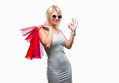 Genç güzel sarışın kadın parmakları, mükemmel sembolü olan ok işareti yapıyor izole arka plan üzerinden Holding alışveriş torbaları satış alışveriş