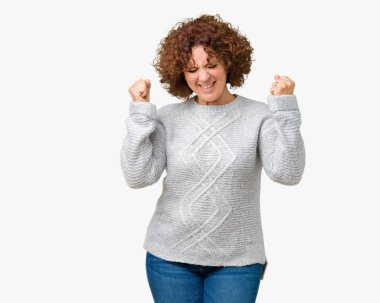 Üzerinde kış kazak giyen güzel orta ager üst düzey kadın gülümseyerek ve başarı için çığlık arka plan çok mutlu ve heyecanlı kaldırdı, silah ile kazanan jest yapıyor izole. Kutlama kavramı.