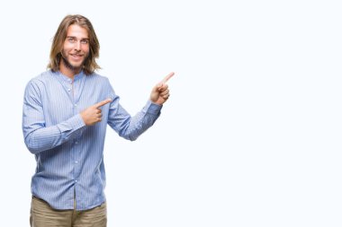 Gülümseyen ve iki elleri ve parmakları ile tarafına işaret kamera bakarak izole arka plan üzerinde uzun saçlı yakışıklı delikanlı.