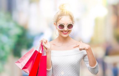 Sürpriz yüz işaret parmağı kendini izole arka plan üzerinde alışveriş torbaları tutan genç güzel sarışın kadın